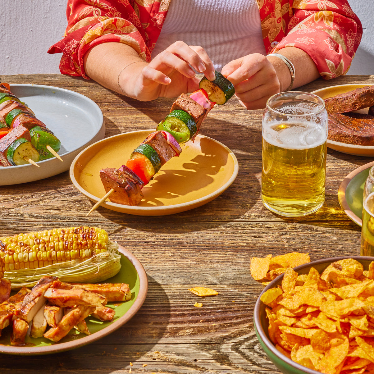 a woman holding a skewer with vegetables and meati classic steak chunks on a yellow plate.